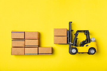Yellow forklift on bright textured background. Logistics concept. Logistics and supply chain management for online shopping concept. Delivery of goods or products to the store worldwide. Cardboard box