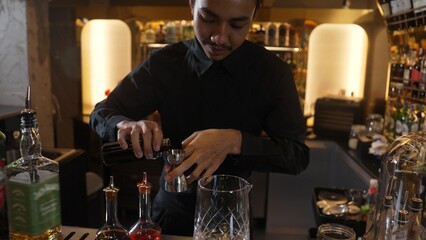 Portrait good looking Asian bartender using jigger measure liquor syrup into mixing glass preparation at luxurious beverage counter bar, neat professional barman costume at nightclub luxury. Vinosity.
