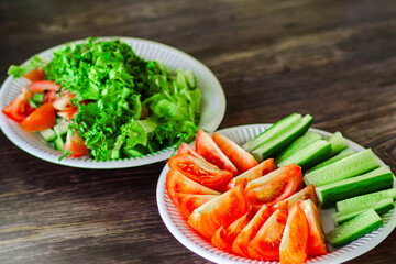 Close-up of fresh cucumber and tomato salad on a white plate placed on a natural wooden table, with focus on vibrant colors and texture of the vegetables.

