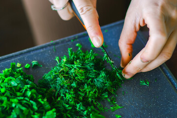 Close-up of hands chopping fresh green dill with a black knife on a wooden cutting board, focused...