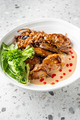A gourmet dish featuring tender grilled chicken served with a creamy sauce, alongside a portion of seasoned grains and fresh greens, elegantly arranged in a modern white bowl on a textured gray surfac