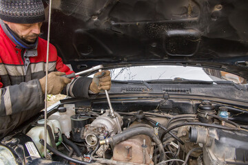 A European man in work clothes repairs a car engine.