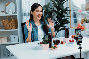 Smiling young beautiful Asian reviewing tasty mixed strawberry and cherry juice detox drinks,...