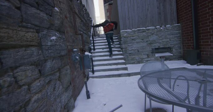 Point of view chasing mysterious person through snowy outdoor corridor as he creates obstacles with chairs