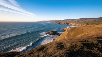 Landscape photograph of a beautiful coastal area. the sky is blue with a few white clouds scattered across it. the horizon line is visible in the distance, and the water is a deep blue-green color.