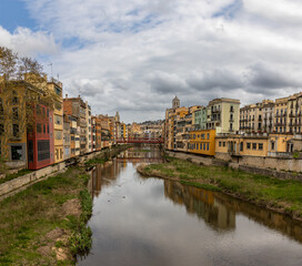 Obraz premium The Onyar River runs through Girona's historic center. The facades of the buildings along the river are painted in warm tones such as yellow, orange, red, and white. Spain