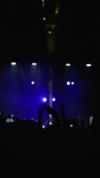 Music light show. Dark silhouette of raised hands of fans in wave motion. Blue and ellow strobe light from stage. Medium close-up shot. Slow motion