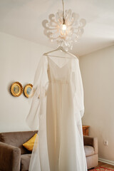White bride dress hanging on a hanger on a chandelier in the room