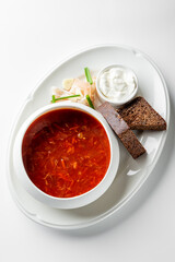 A bowl of rich, red borscht soup served with sour cream, dark rye bread, and pickled vegetables. A comforting traditional dish, perfect for a cozy meal.