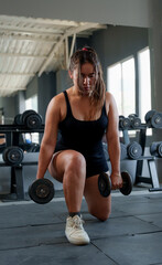 Determined young woman doing dumbbell lunges at the gym, focusing on strength training