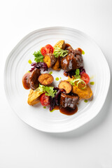 A gourmet dish featuring tender meat served with golden potatoes, cherry tomatoes, and a drizzle of sauce. Garnished with fresh greens, it's a feast for the eyes and palate.
