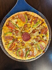 Gourmet Mixed-Topping Pizza with Sausage Slices, Green Peppers, Sweet Corn, and Salami Centerpiece, Freshly Baked and Served on a Dark Surface.