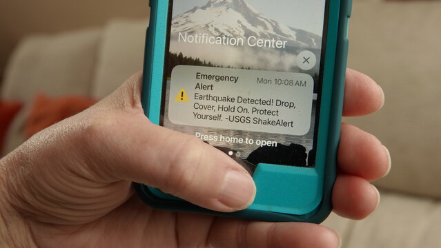 Close up of a hand holding a phone with an emergency earthquake alert displayed on screen