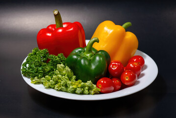 Fresh colorful bell peppers, cherry tomatoes, and herbs on a white plate, healthy food ingredients.