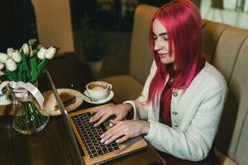 A woman with red hair is sitting with a laptop in a cafe