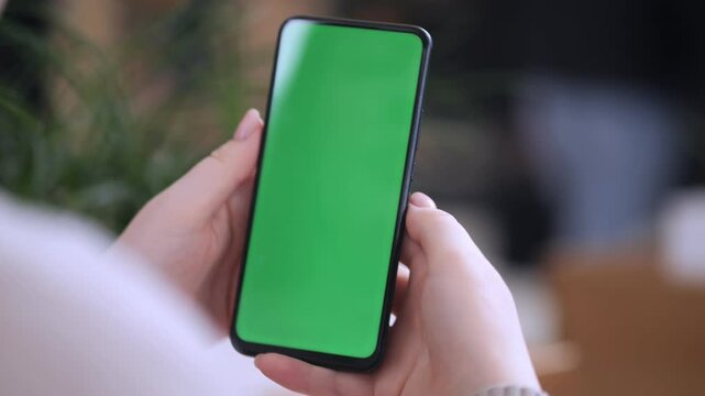 Person is holding a green phone. The phone is turned off and has a green screen. The person is looking at the phone with a curious expression