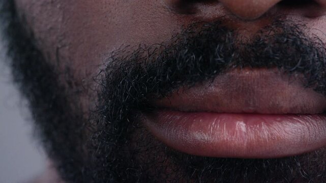 Detailed close-up view of african man face lips and beard isolated on grey background. Portrait of handsome young emotionless black man.