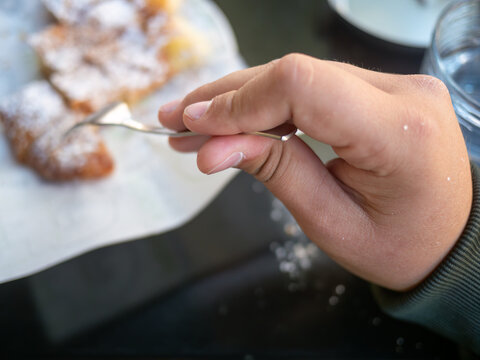Closeup of hands eating traditional Greek bougatsa, a sweet cream pie pastry with filo dough, dusted with powdered sugar and cinnamon. Popular breakfast or snack from Thessaloniki and Serres, Greece.