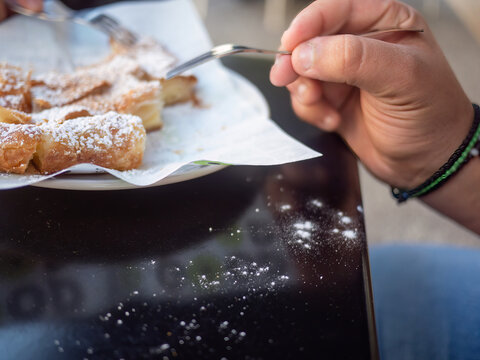 Closeup of hands eating traditional Greek bougatsa, a sweet cream pie pastry with filo dough, dusted with powdered sugar and cinnamon. Popular breakfast or snack from Thessaloniki and Serres, Greece.