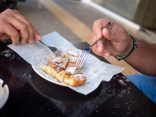 Closeup of hands eating traditional Greek bougatsa, a sweet cream pie pastry with filo dough, dusted with powdered sugar and cinnamon. Popular breakfast or snack from Thessaloniki and Serres, Greece.