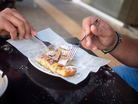 Closeup of hands eating traditional Greek bougatsa, a sweet cream pie pastry with filo dough, dusted with powdered sugar and cinnamon. Popular breakfast or snack from Thessaloniki and Serres, Greece.