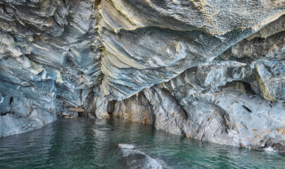 Interior of the flooded Marble Caves, unique rock formations in the General Carrera Lake, Chile. The walls of the caves have swirling mineral patterns. Turquoise water fills the caves with blue light.