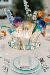 Plates with folded napkins and cutlery stand on the table near a bouquet of flowers