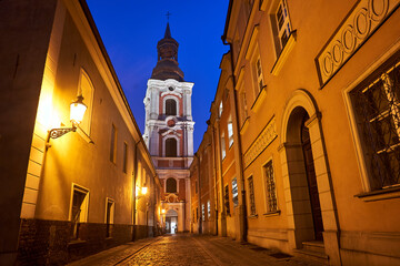 cobbled street and bell tower of a baroque church at night in the city of Poznan
