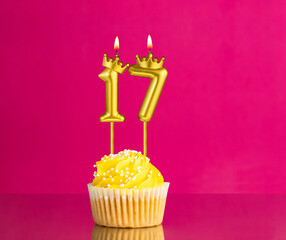 Yellow birthday cupcake with a number 17 candle - Birthday card on a pink background