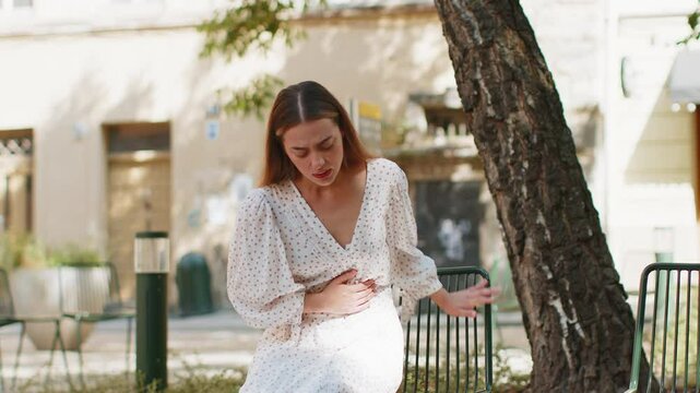 Caucasian young woman traveler feeling sudden strong abdominal stomach ache gastritis problem. Upset tourist lady having symptom poisoning diarrhea indigestion peptic ulcer pancreatitis on city street