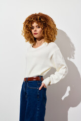 Woman in white sweater and blue jeans against a plain white background, exuding confidence and...