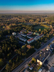 Aerial view of Stąporków, Poland, with apartment buildings nestled among forested areas, showcasing the balance of urban life and nature during golden hour.