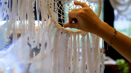 Woman making dreamcatcher from threads, feathers, beads and silk ribbons, making home decor items,...