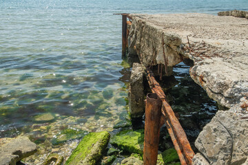 Dilapidated concrete structure extends into the clear, green-tinted sea, with vibrant green algae clinging to the submerged portions