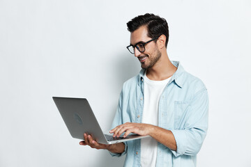 Smiling young man with eyeglasses hold laptop computer type on keyboard wear casual light blue...