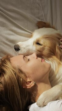 A young woman relaxes on a comfy couch, her Corgi curled up on her lap. She gently strokes its fur, whispering softly as the pup rests in peaceful bliss. The moment glows with warmth, love, and the