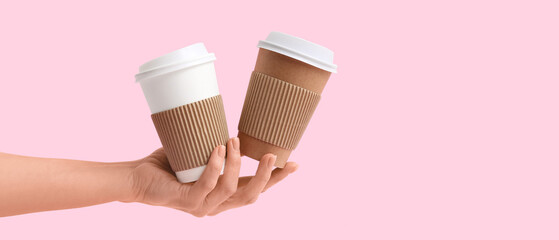 Female hand with disposable cups of coffee on pink background