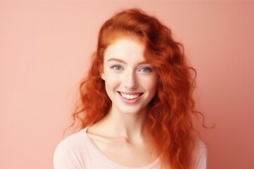 Naklejka premium A portrait of a young woman with vibrant red curly hair and a bright smile against a soft pink background.