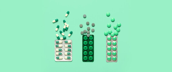 Different pills in blister packs on green background, top view