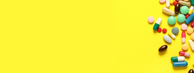 Different colorful pills on yellow background with space for text