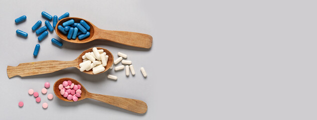 Wooden spoons with different pills on grey background with space for text