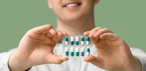 Man holding pills on green background, closeup