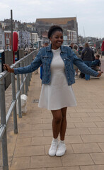 Weymouth Dorset England UK. 12.04.2025.  Young African woman wearing a short white dress on the waterfront in the holiday resort of Weymouth.