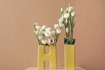 Vases in shape of word HI with beautiful eustoma flowers on table near color wall
