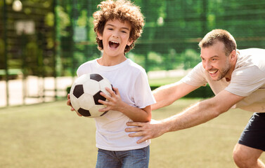 Bonding. Portrait in action of joyful dad and son playing soccer together, man trying to catch the ball, selective focus
