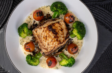 Grilled fish fillet, topped with a rich creamy sauce, pairs beautifully with vibrant broccoli and roasted cherry tomatoes, creating a delightful and nutritious meal experience