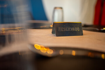 Metal reserved sign standing on an elegant restaurant table, creating an inviting atmosphere with soft, warm lighting and blurred tableware in the foreground and background