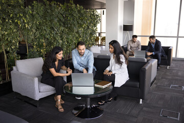 Group of multinational young teammates sit at table with laptop, deeply engaged in discussion or...