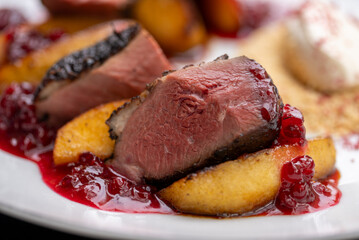 Close up of juicy, seared duck breast, served with roasted peach slices, tart cranberry sauce, and creamy polenta, offering a delightful combination of flavors and textures