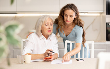 Elderly woman and adult woman discussing agreement while sitting at table in kitchen